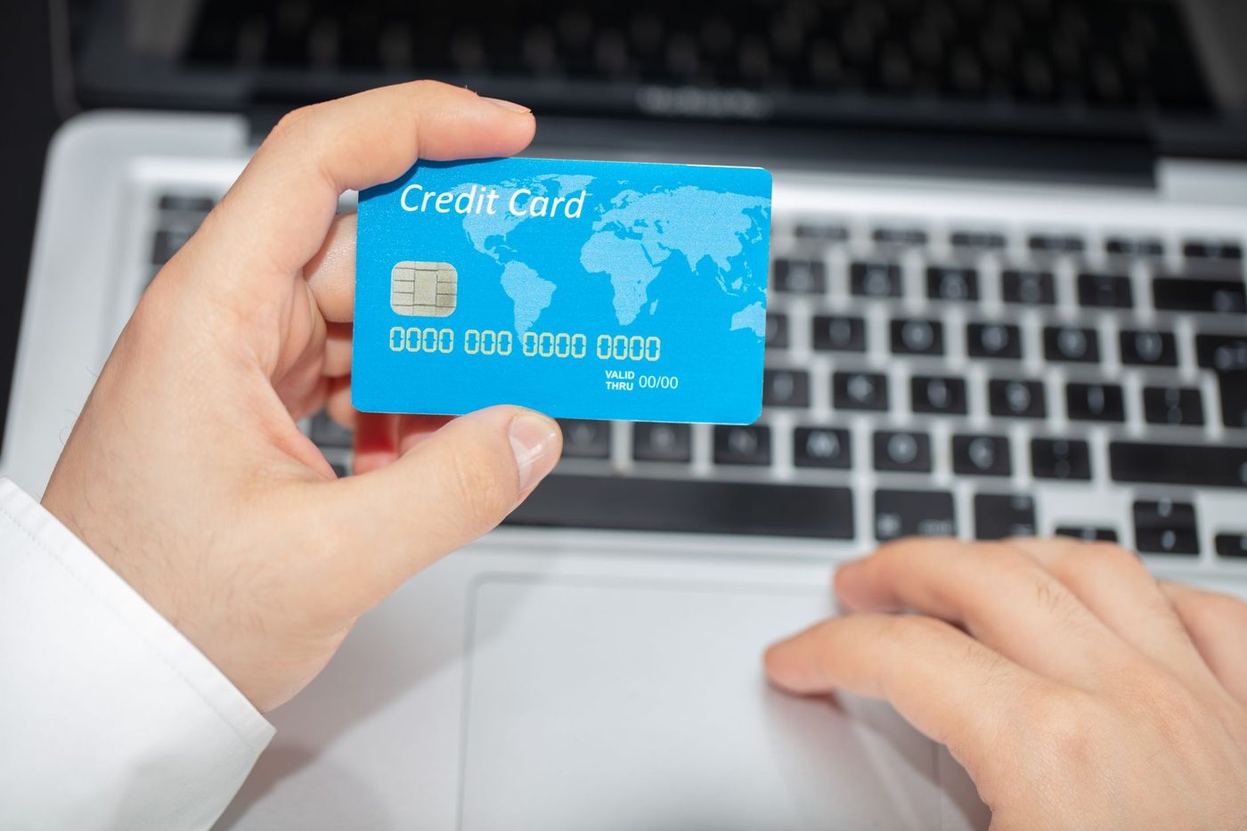 A person holding a credit card beside a laptop